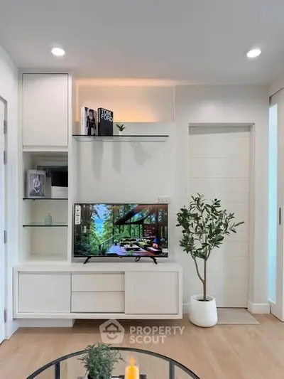 Modern living room with sleek white cabinetry and a flat-screen TV, featuring stylish decor and a potted plant.