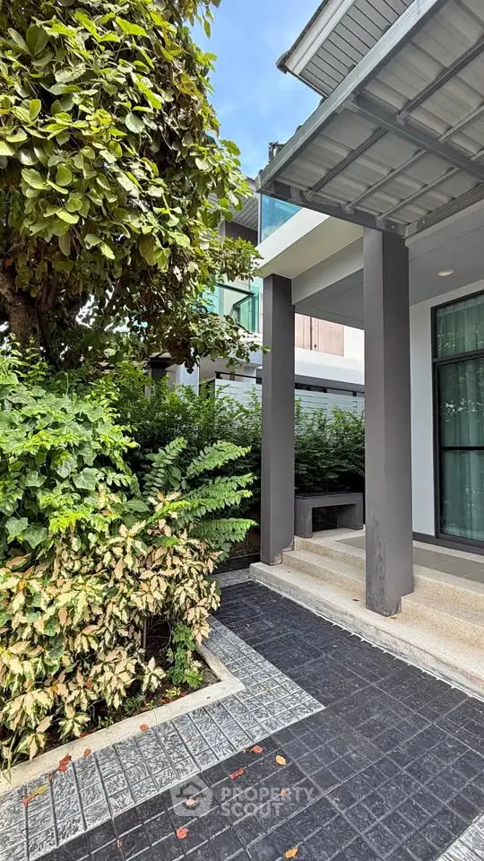 Modern building entrance with lush greenery and sleek architectural design.
