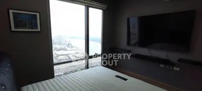 Modern bedroom with large window offering stunning city and river views, featuring a wall-mounted TV.