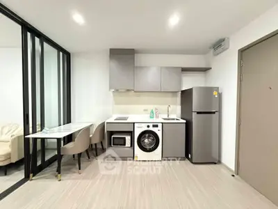 Modern kitchen with sleek appliances and dining area in open layout apartment.