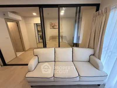 Modern living room with elegant sofa and glass partition leading to bedroom, showcasing contemporary design.