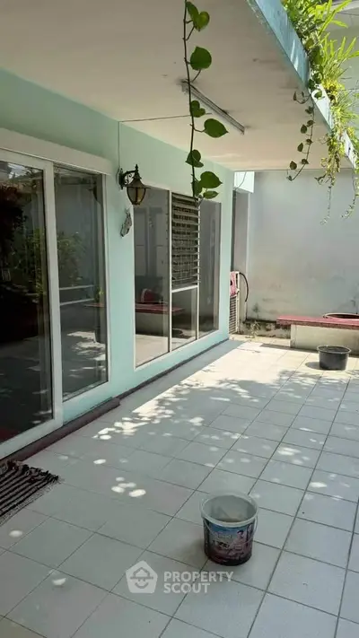 Spacious tiled patio with sliding glass doors and lush greenery, perfect for outdoor relaxation.