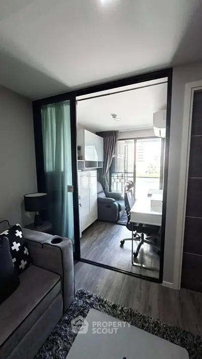 Modern living room with glass partition leading to a stylish study area, featuring sleek furniture and natural light.