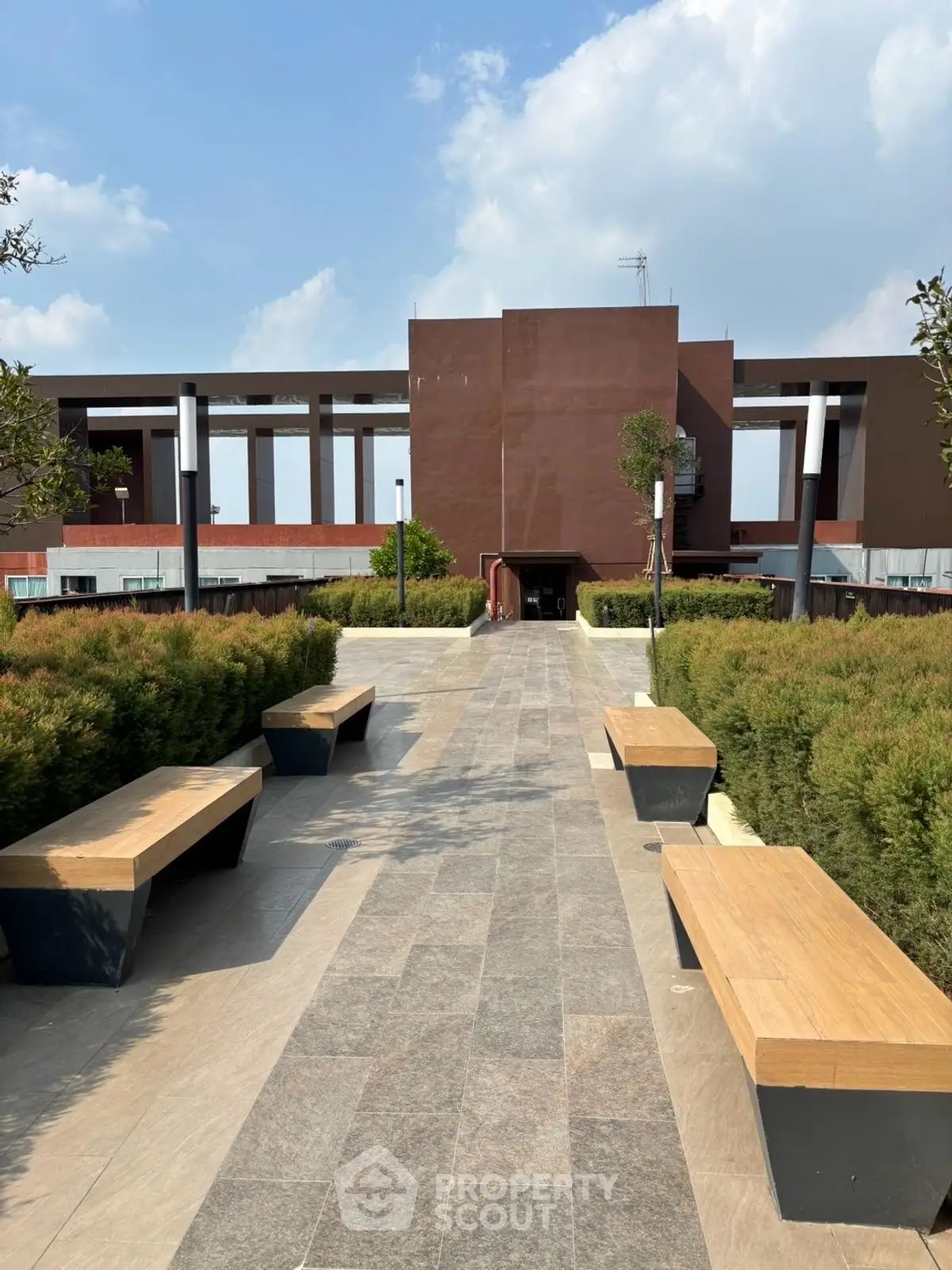 Modern building entrance with landscaped pathway and benches under a clear blue sky.