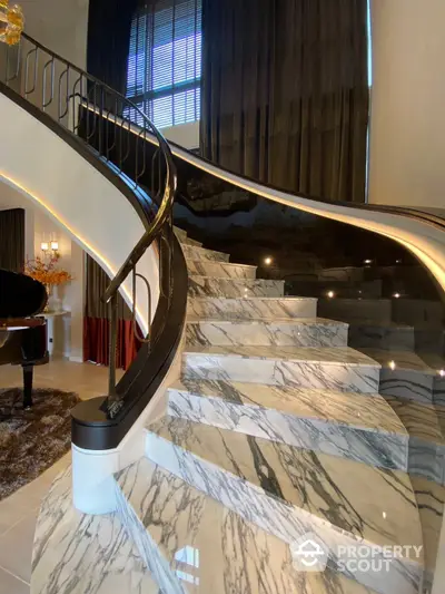 Luxurious marble staircase with elegant wrought iron railing, leading to an opulent living space with grand piano and sophisticated decor.