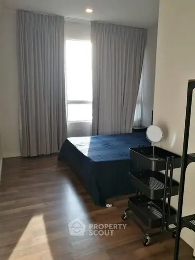 Cozy bedroom with wooden flooring and natural light from large window.