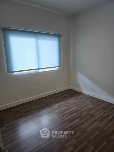Spacious empty room with wooden flooring and large window with blinds.