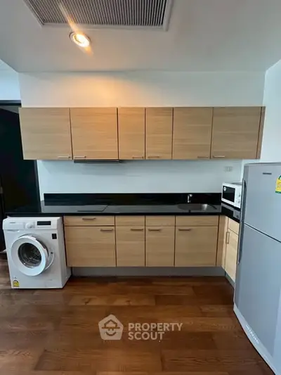 Modern kitchen with wooden cabinets, washing machine, and fridge in a sleek apartment.