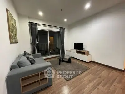 Modern living room with cozy sofa and TV, featuring wooden flooring and balcony access.