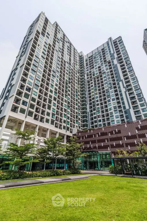 Modern high-rise residential building with lush green lawn and contemporary design.