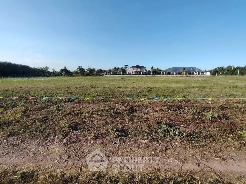 Expansive land plot with distant view of a house and mountains, ideal for development.