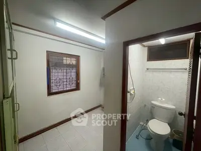 Compact bathroom with tiled floor and window, featuring toilet and shower area.