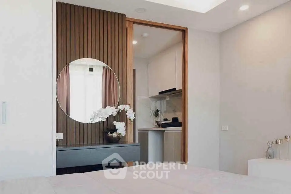 Modern bedroom with elegant decor and stylish mirror, featuring a glimpse of a compact kitchen area.