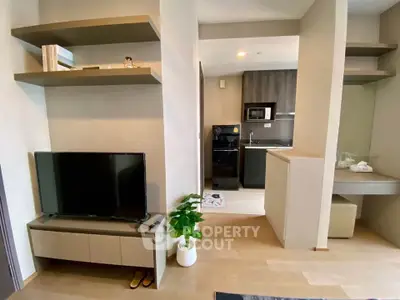 Modern living room with TV and open kitchen layout, featuring sleek shelves and stylish decor.