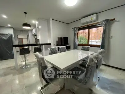 Modern dining area with sleek white table and chairs, open kitchen layout, and natural light.