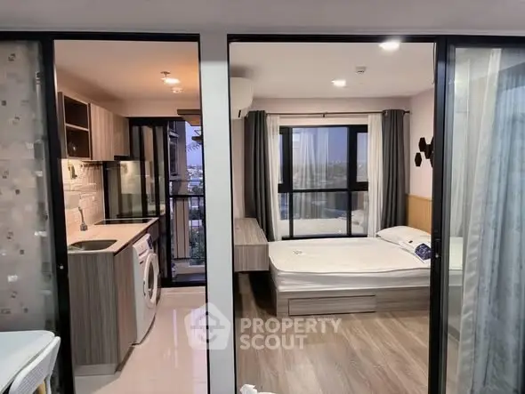 Modern studio apartment with kitchen and bedroom, featuring large windows and stylish decor.