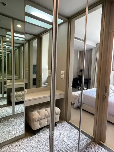 Luxurious bedroom with mirrored closet and plush ottoman in modern apartment.