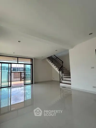 Spacious modern living room with staircase and large windows leading to balcony.