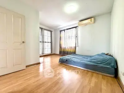 Spacious bedroom with wooden flooring and natural light, featuring a minimalist design and air conditioning.
