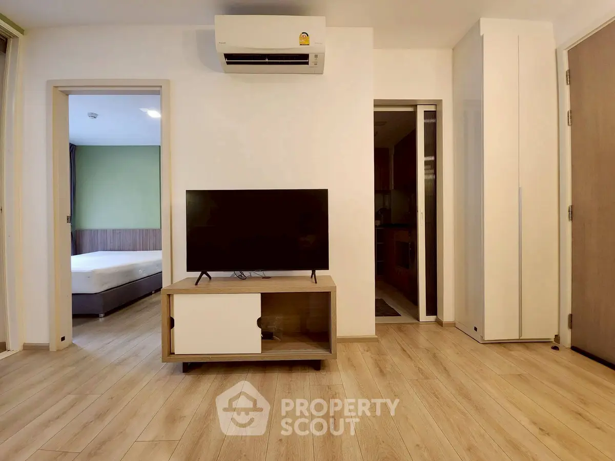 Modern living room with TV and air conditioning, featuring wooden flooring and minimalist design.