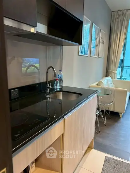 Modern kitchen with sleek black countertop and cozy living area in open layout apartment.