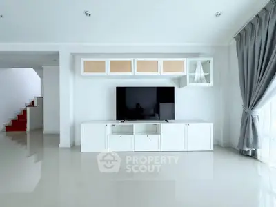Spacious modern living room with sleek white entertainment unit and large TV, featuring elegant curtains and glossy flooring.