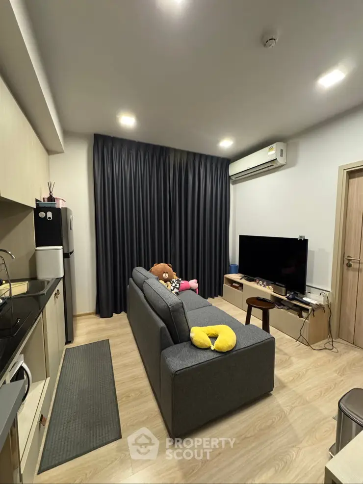 Modern living room with sleek design, featuring a cozy sofa, large TV, and stylish kitchen area.