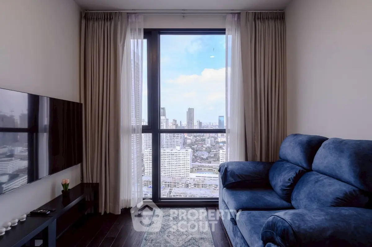 Modern living room with stunning city view through large window, featuring plush blue sofa and wall-mounted TV.