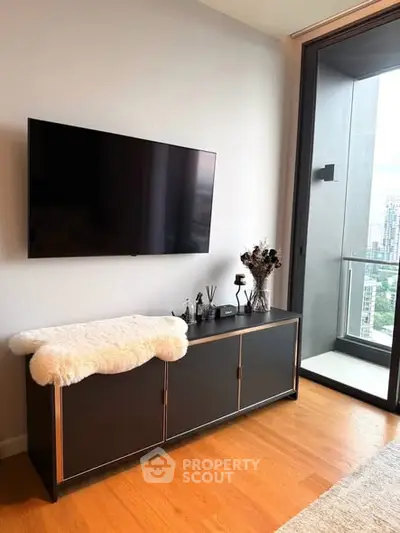 Modern living room with sleek TV setup and balcony view in urban apartment.