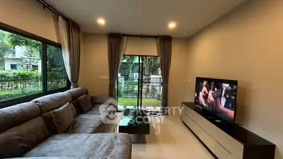 Modern living room with large sofa and TV, overlooking a garden view.