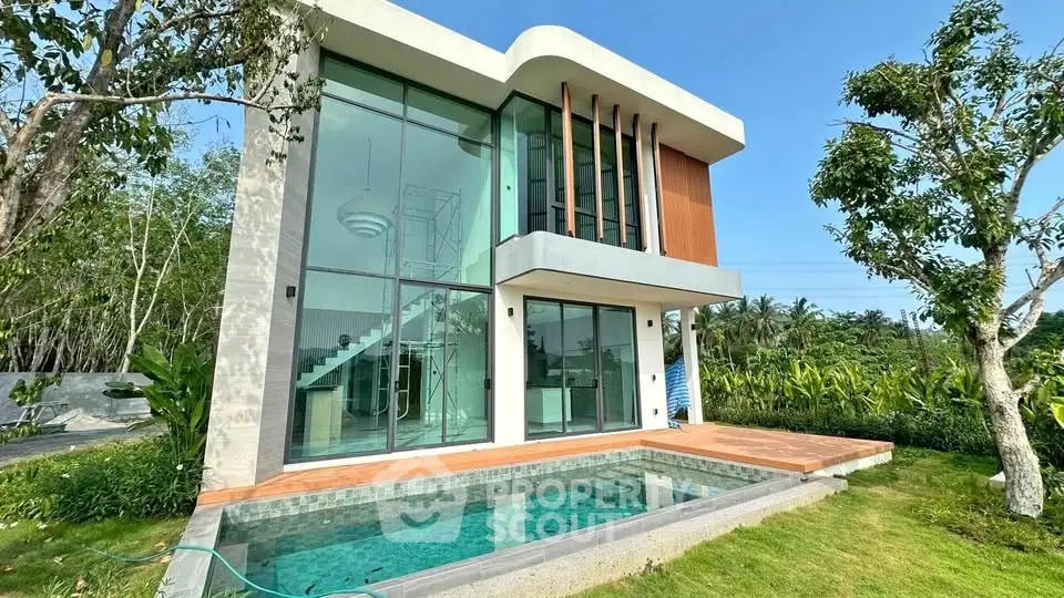 Modern two-story house with large windows and private pool in lush green setting.