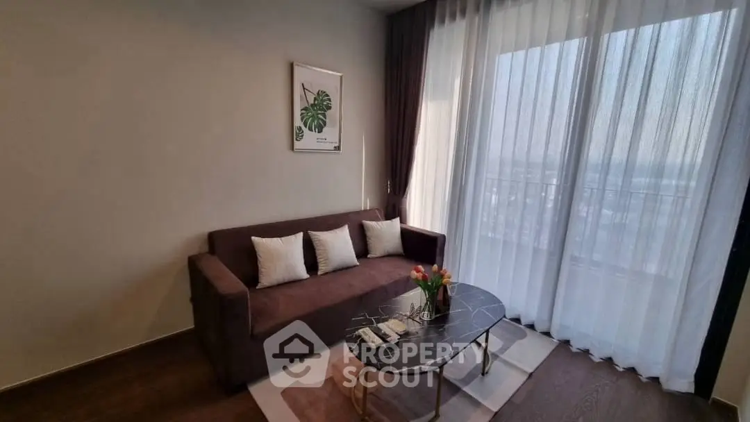 Stylish living room with modern sofa and elegant coffee table, featuring large window with sheer curtains.