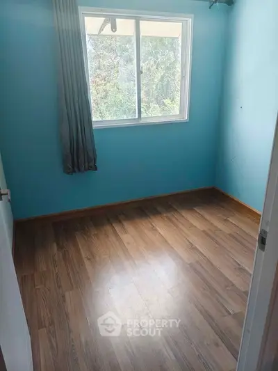 Spacious empty bedroom with wooden flooring and large window offering natural light.