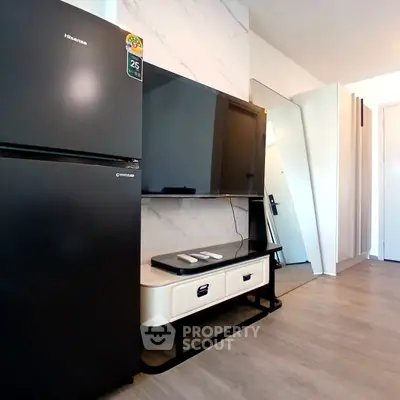 Modern living room with sleek black fridge and large flat-screen TV on stylish stand.