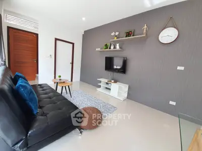 Modern living room with sleek black sofa and wall-mounted TV, featuring stylish decor and natural light.