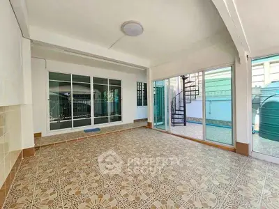 Spacious tiled room with large windows and spiral staircase access to outdoor area.