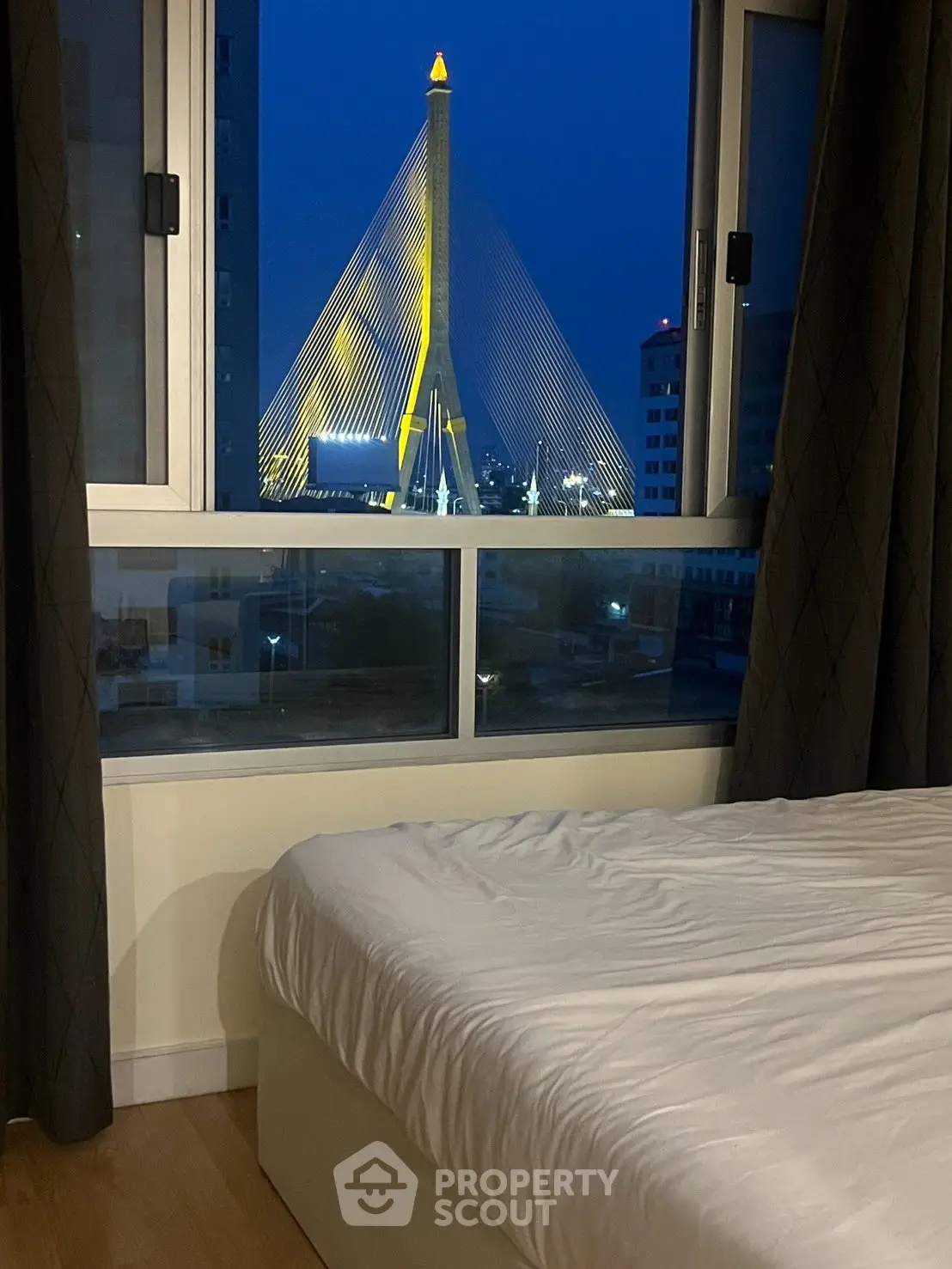 Stunning bedroom with a breathtaking view of an illuminated cable-stayed bridge at night.