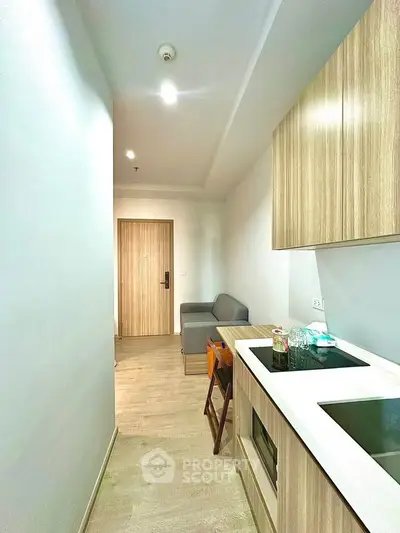 Modern compact kitchen with wooden cabinets and cozy living area in a stylish apartment.