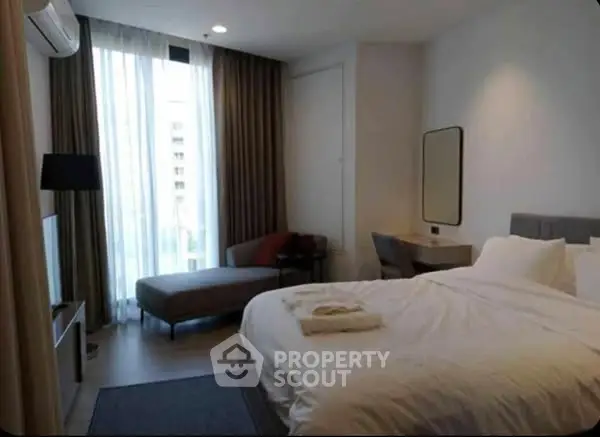 Modern bedroom with cozy bed, large window, and stylish decor in a high-rise apartment.