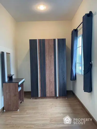 Modern bedroom with stylish wardrobe and vanity set, featuring wooden flooring and natural light.