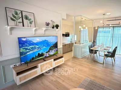 Modern living room with open kitchen and dining area, featuring stylish decor and large TV.