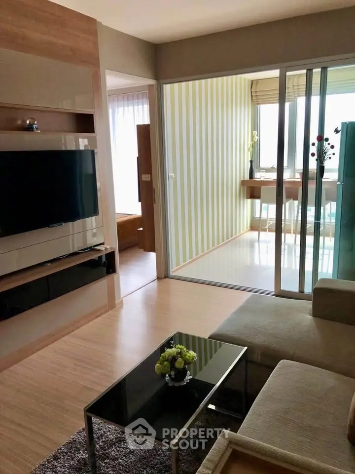 Modern living room with sleek TV setup and cozy seating area, leading to a bright balcony with stylish decor.