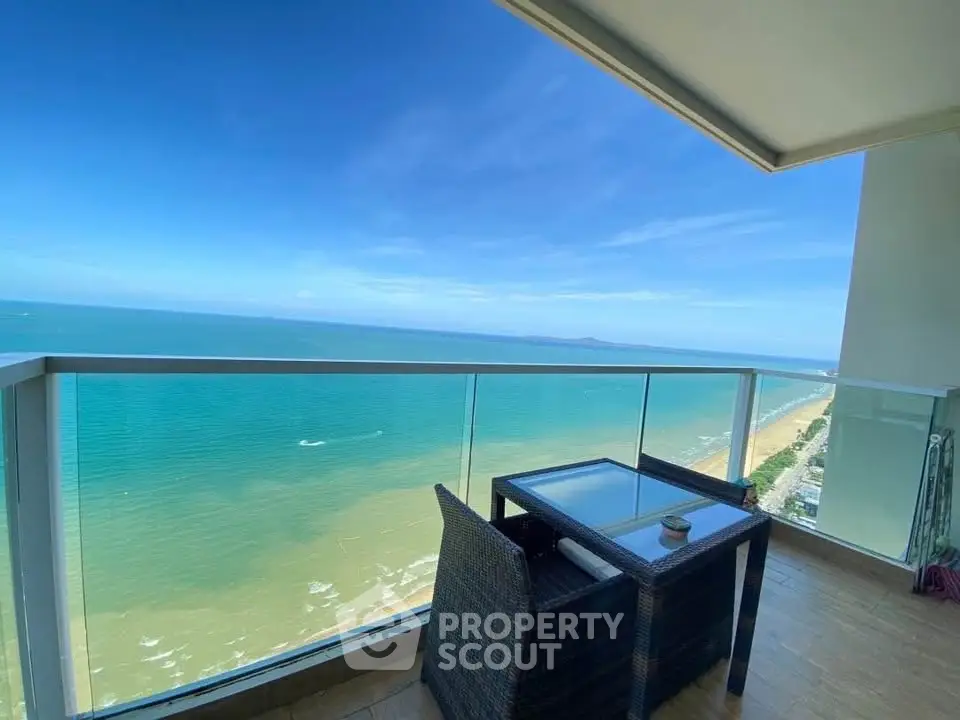 Stunning ocean view from a modern balcony with glass railing and cozy seating area.