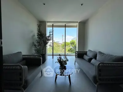 Modern living room with large windows and stylish furniture overlooking greenery.