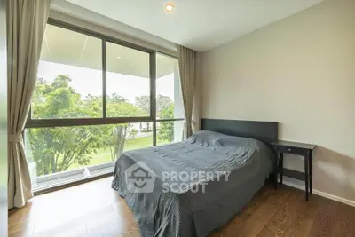 Bright bedroom with large window and garden view, featuring modern decor and wooden flooring.