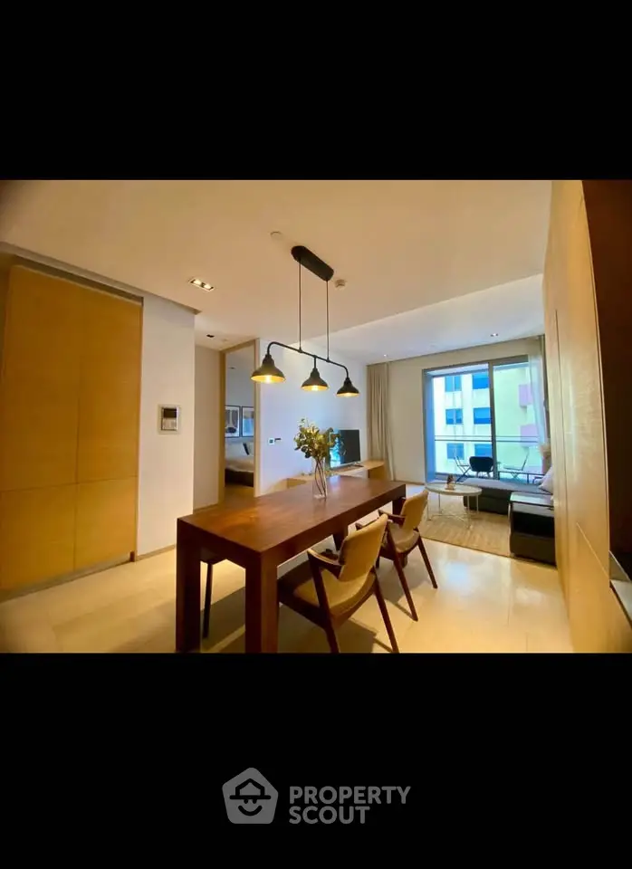 Modern dining area with wooden table and chairs, stylish lighting, and cozy living space.