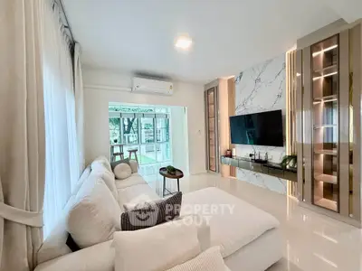 Luxurious modern living room with plush white sofa, marble accent wall, and large windows offering garden views.