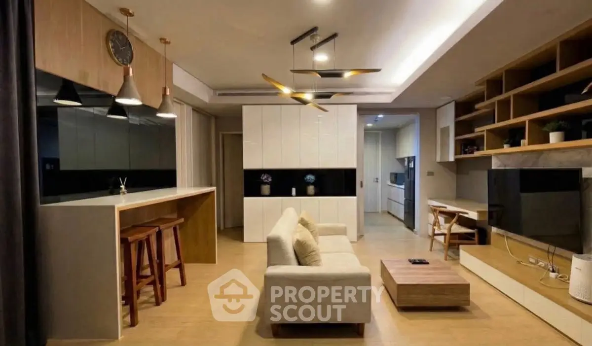 Modern living room with open kitchen, stylish lighting, and cozy seating area.