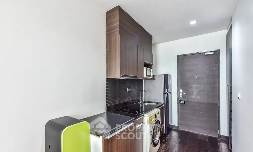 Modern kitchen with sleek cabinets, washing machine, and fridge in compact layout.