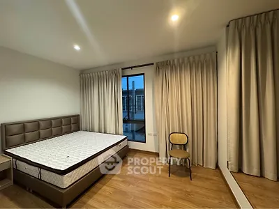 Spacious bedroom with wooden flooring and large window, featuring a comfortable bed and elegant curtains.